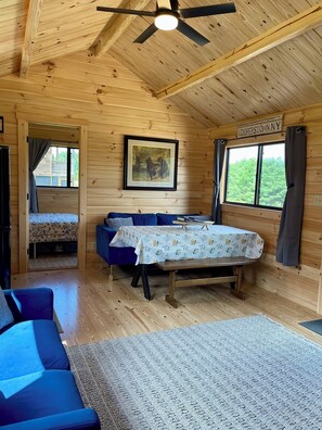 A cabin interior with a bed, blue sofa, and a dining table. - Cooperstown Double Play Glenview Cabin C (Cooperstown)