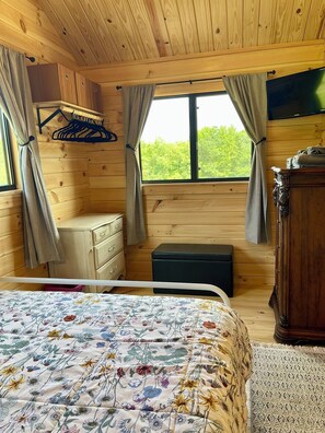 A wooden cabin bedroom with a bed, dresser, and a window with curtains.