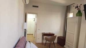Une chambre d’hôtel avec un lit, un bureau, une chaise, une armoire et une salle de bain visible à travers une porte ouverte.