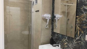 Une salle de bain dotée d’une douche à parois de verre, d’un lavabo blanc et d’un miroir orné d’un motif de feuilles sur le mur.