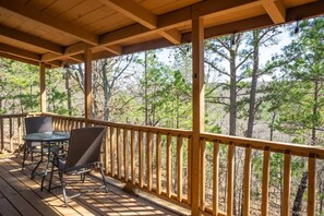 A wooden deck with a table and chairs, surrounded by a wooden railing, overlooking a forested area.