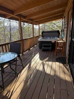 A wooden deck with a hot tub, a table, and chairs.