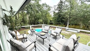 Eine Holzterrasse mit Gartenmöbeln, einem Pool und Blick auf ein bewaldetes Gebiet.