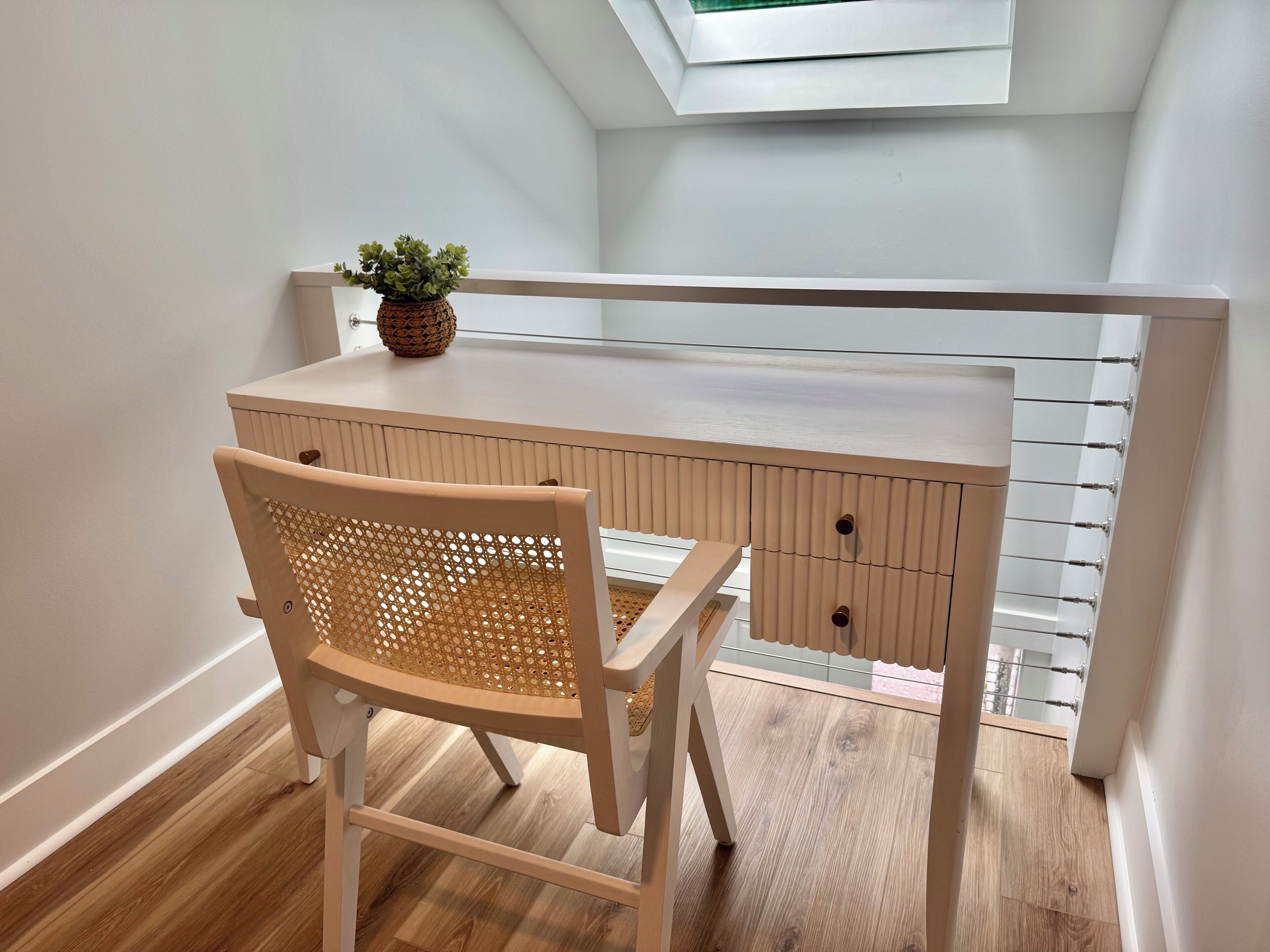 A corner desk with a chair, a small plant, and a skylight.