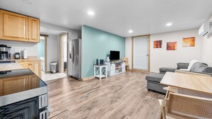 Een moderne keuken met houten kastjes, een inbouwfornuis en een eethoek met een tafel en stoelen.