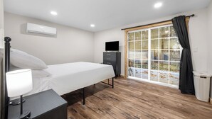 Een slaapkamer met een bed, nachtlampje, televisie, dressoir en een raam met gordijnen.