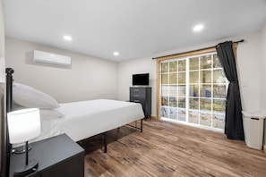 A bedroom with a bed, bedside lamp, TV, dresser, and a window with curtains.