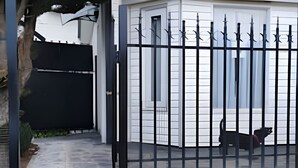 Ett hus med en grind, en täckt veranda och en hund som syns genom grinden.