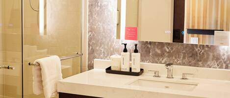 A modern bathroom with a glass shower enclosure, a marble backsplash, a large mirror, and a vanity with a towel rack and toiletries.