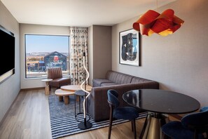 A modern living room with a sofa, two chairs, a small table, a large window with a view of a building, and a unique pendant light. - Tempo By Hilton Manassas (Manassas)