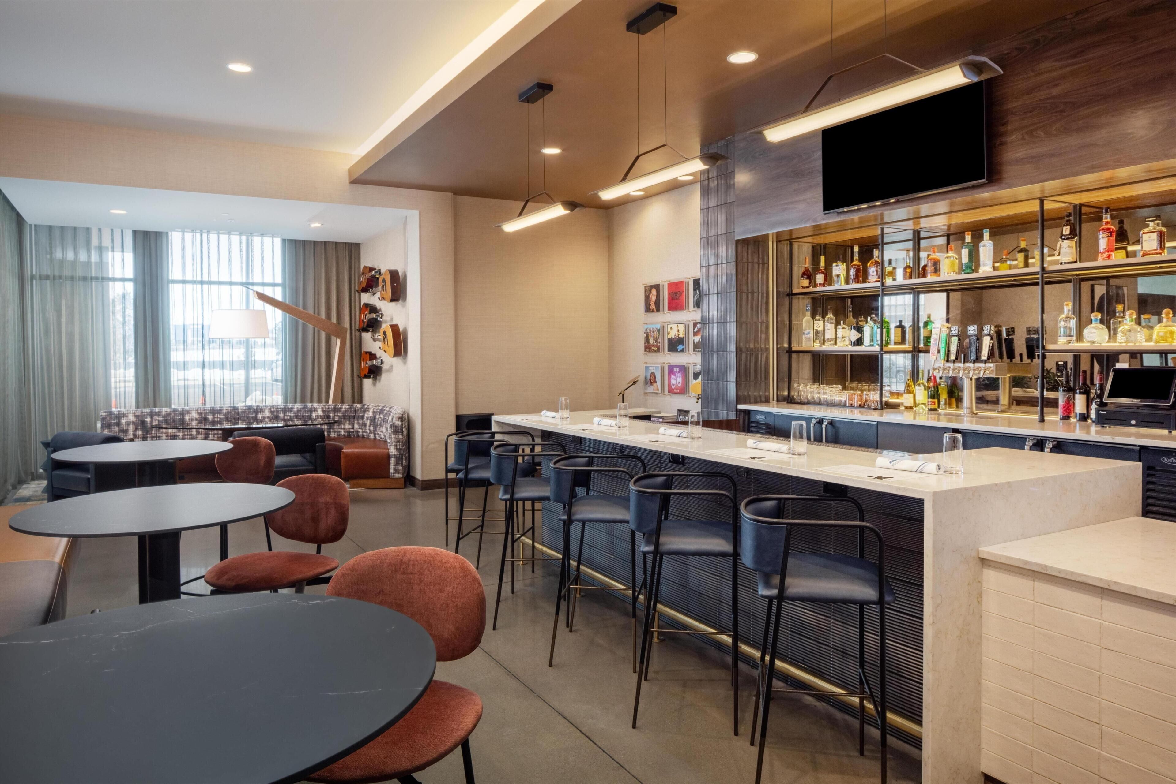 A modern bar area with a long counter, multiple bar stools, and a variety of bottles and glasses.