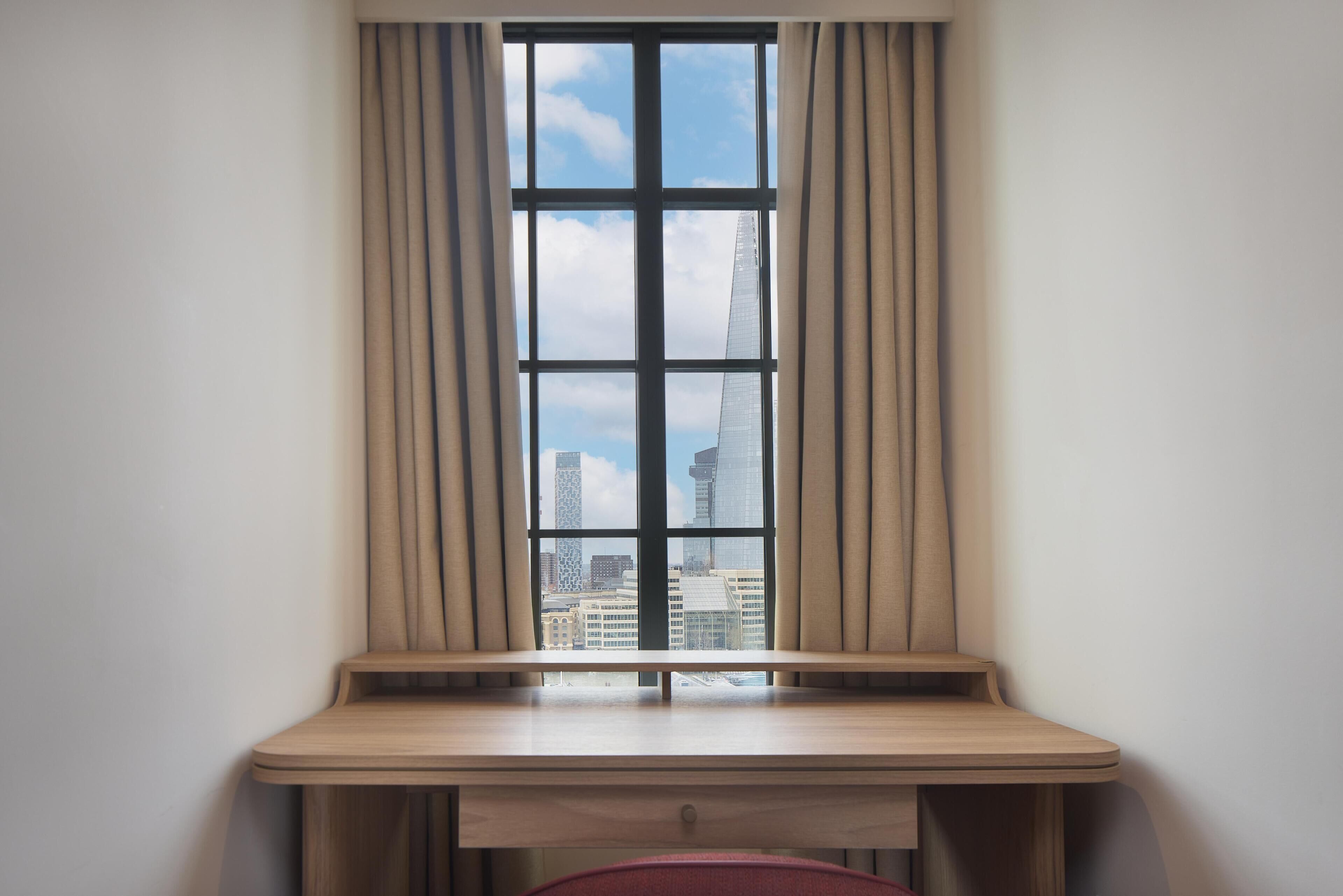 Mesa no canto com vista para a paisagem urbana através de uma janela com cortinas.