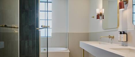 Un baño moderno con cabina de ducha de vidrio, bañera y un espejo grande con luces empotradas.