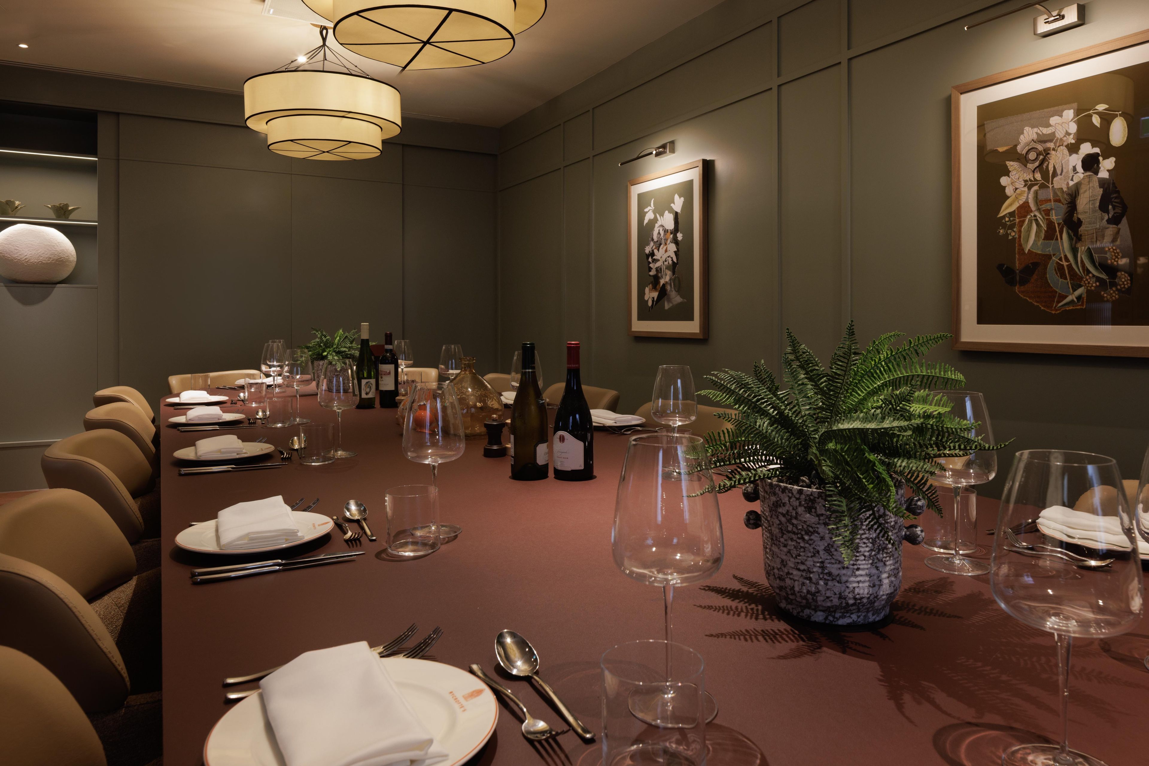 A conference room with a long table set for a meeting, equipped with chairs, plates, cutlery, and wine glasses.