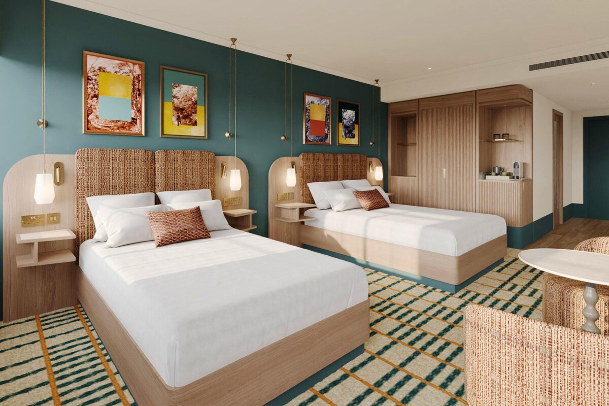 A hotel room with two beds, a small kitchenette, a seating area, and artwork on the walls.