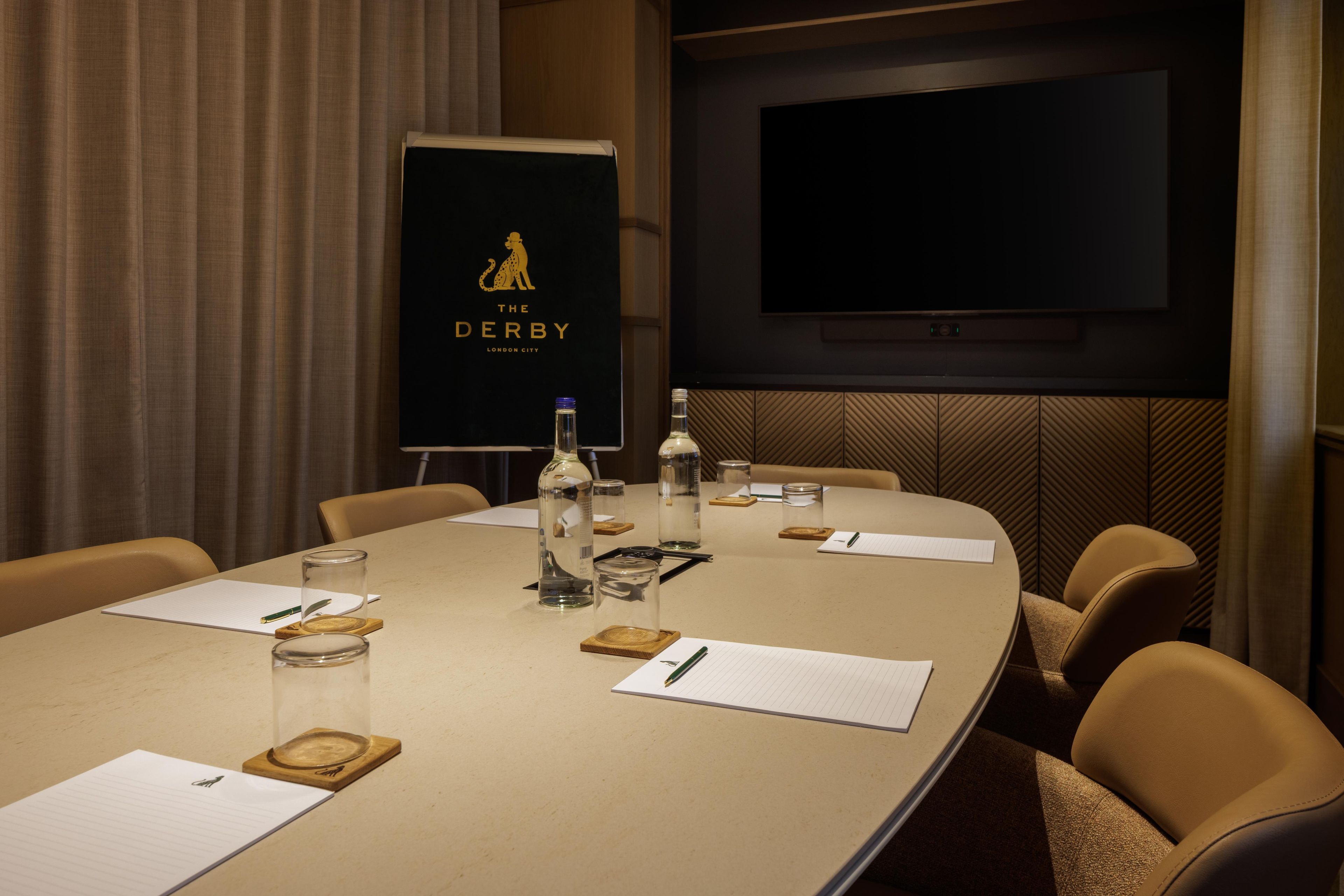 A conference room with a long table, chairs, a projector screen, and a television.
