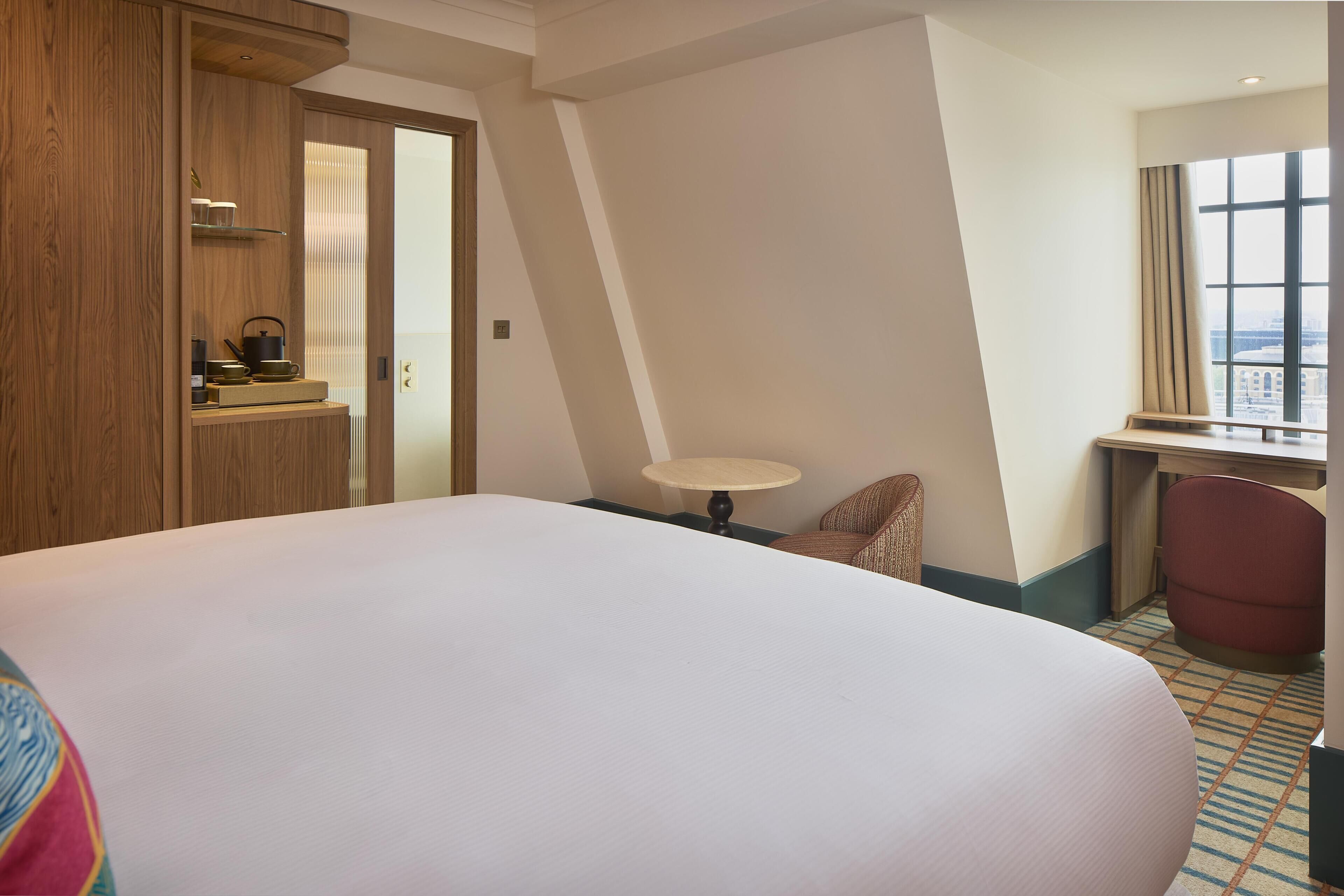 A hotel room with a large bed, a desk, a chair, a small table, and a window with a view.