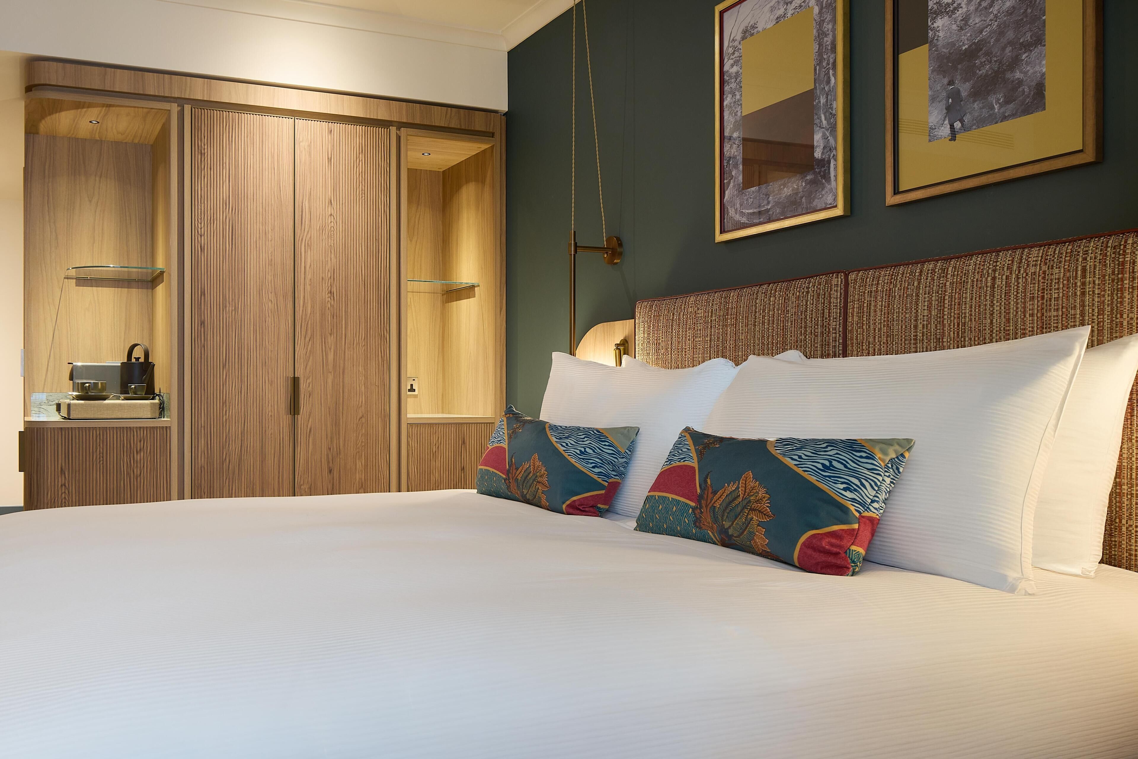 A hotel room with a large bed, wooden wardrobe, and a small bedside table with a lamp.