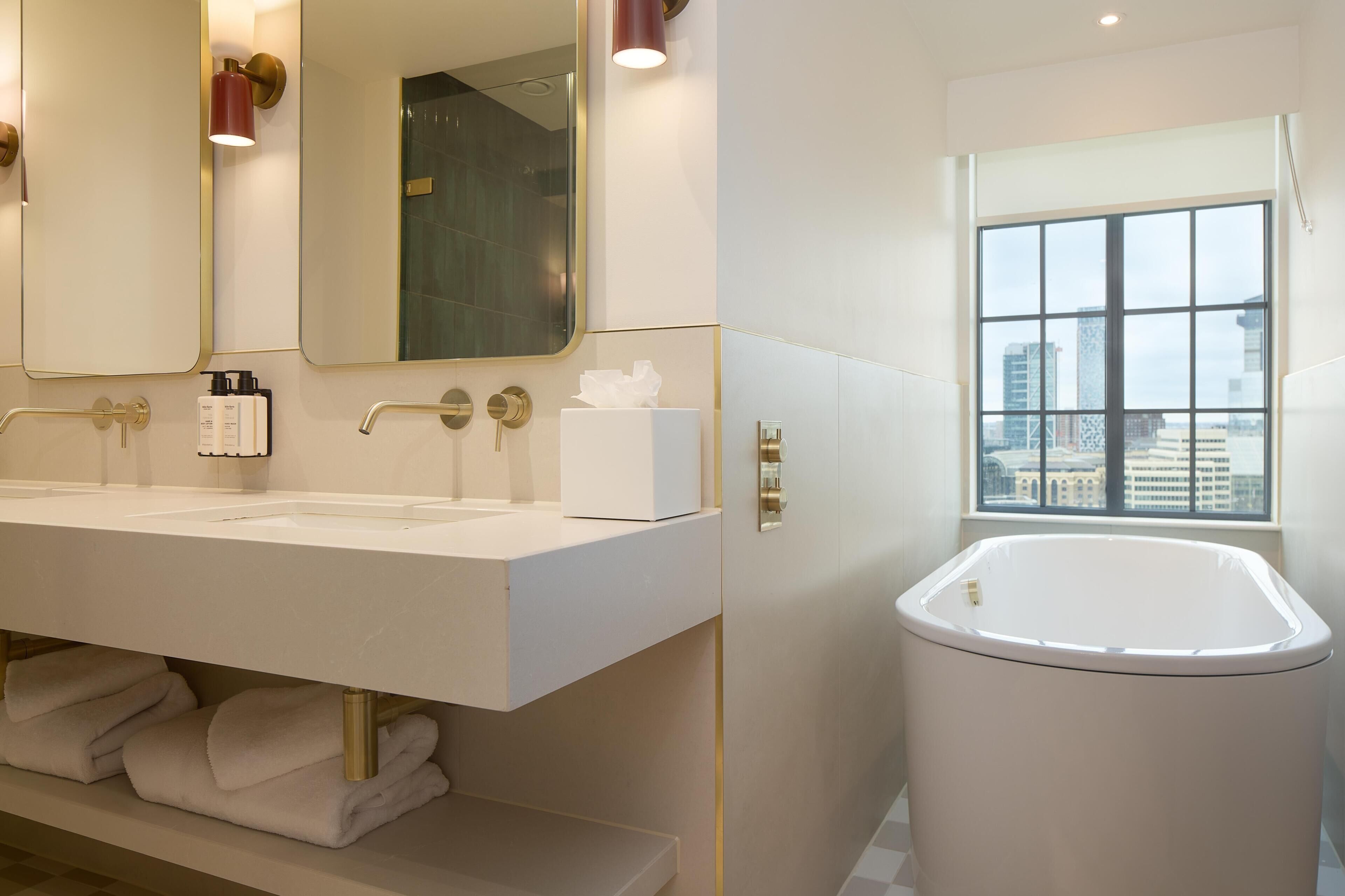 A bathroom with a large mirror, two sinks, a bathtub, and a window with a city view.