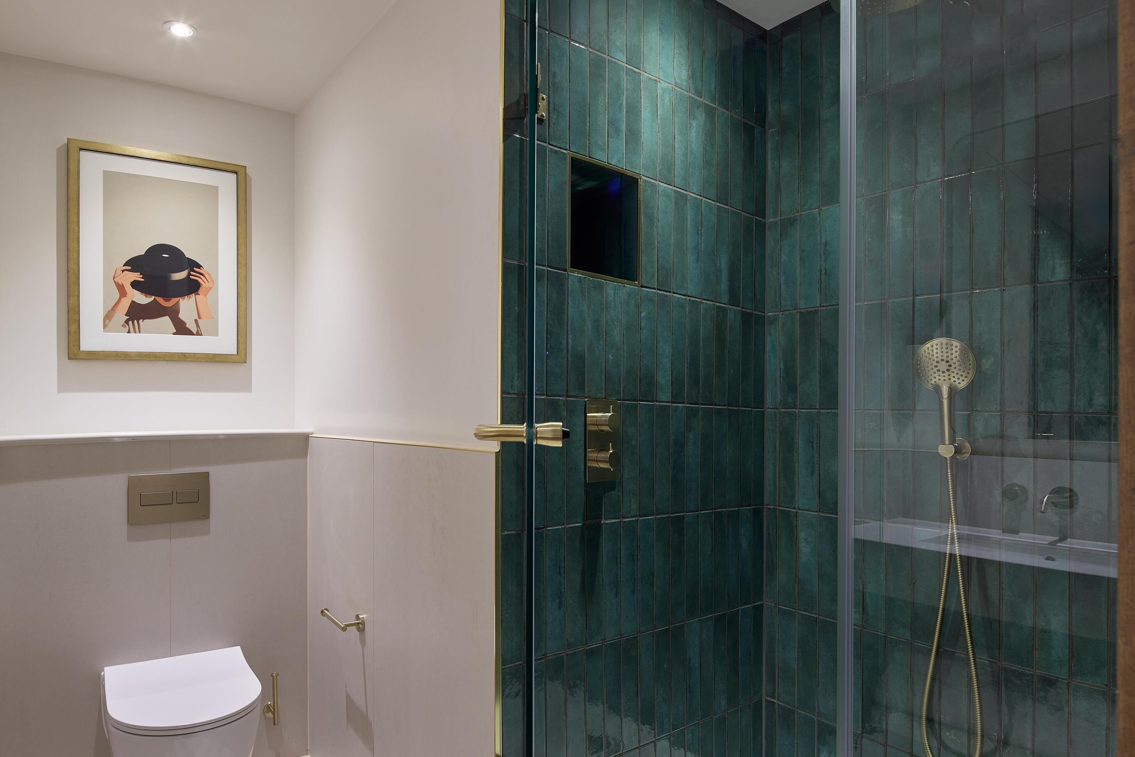 Un baño con inodoro, ducha con puerta de cristal y un cuadro en la pared.