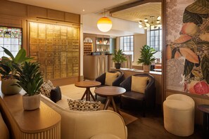 A hotel lobby with a check-in desk, seating area, and a large wall of lockers. - The Derby London City, Curio Collection By Hilton (London)