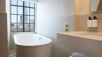 Un baño moderno con bañera, una ventana con vista a la ciudad, un lavabo y artículos de tocador en la pared.