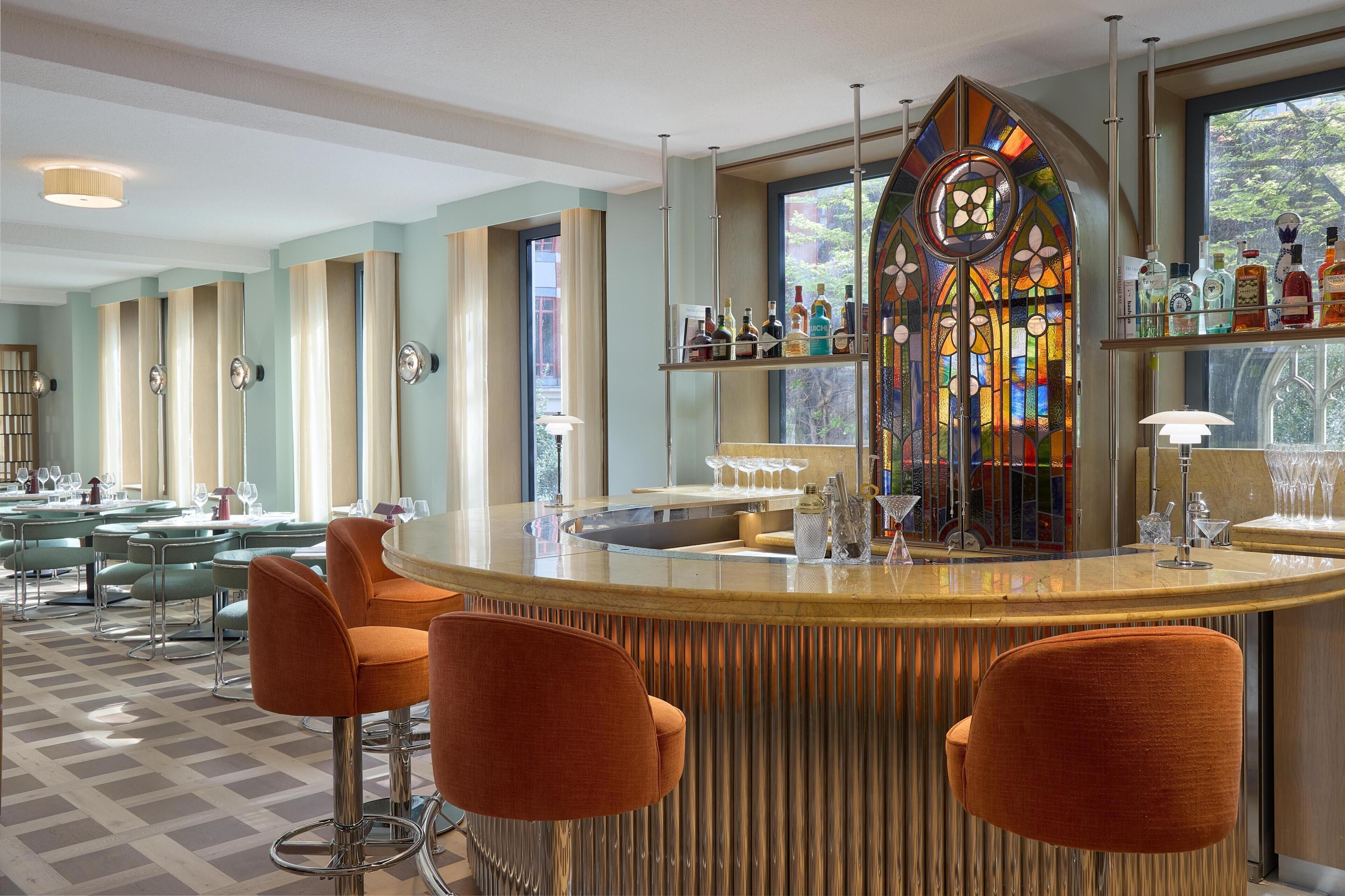 A bar area with a stained glass window, bar stools, and a view through the window.