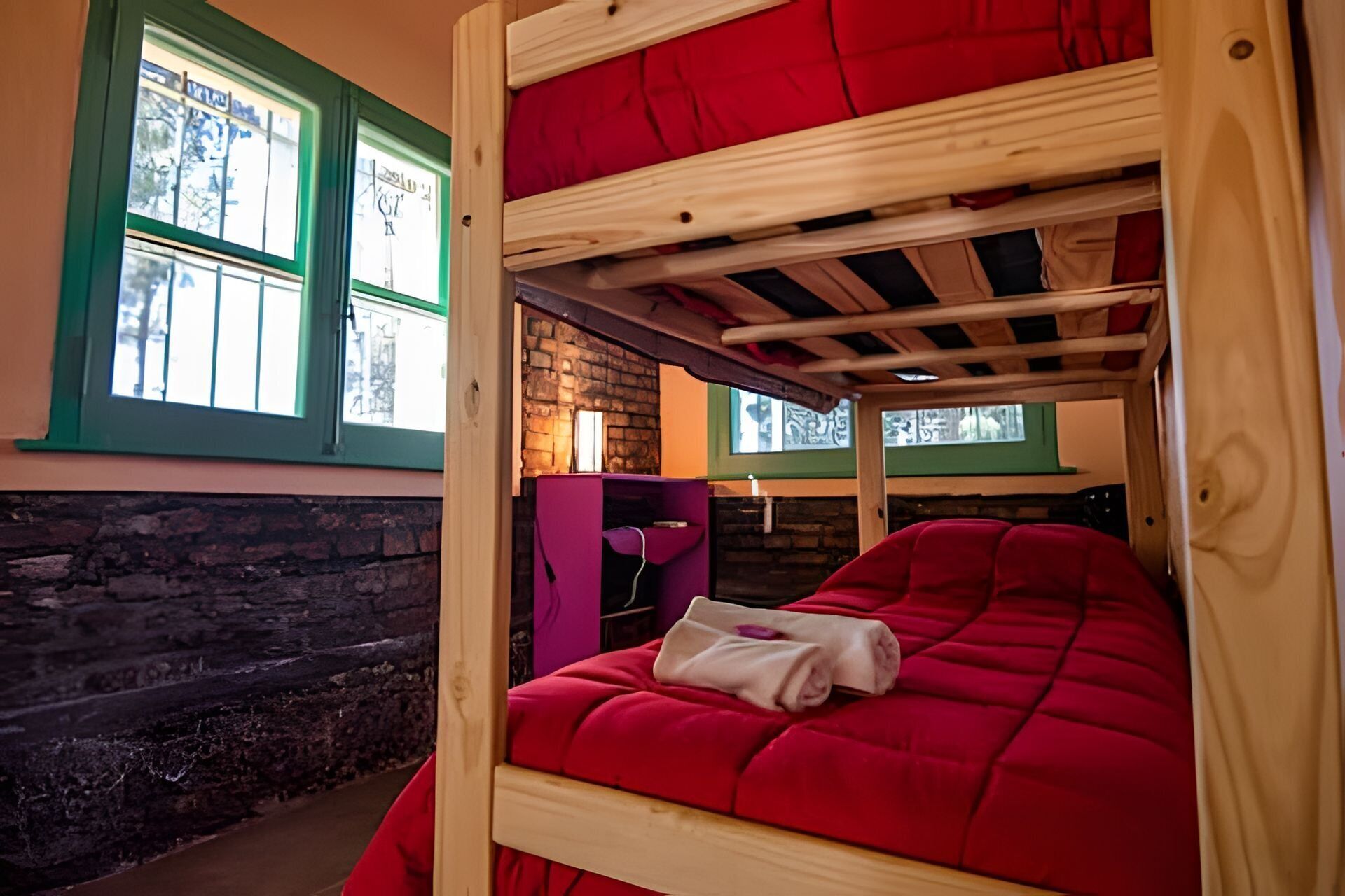 A bunk bed with red bedding in a room with stone walls and green window frames.