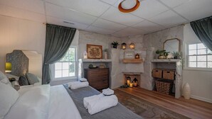 A bedroom with a large bed, a dresser, a fireplace, and a window with curtains. - Cozy 3BR Home | KING Bed | ONLY 8-Min to LU! (Lynchburg)