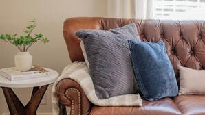 A brown leather sofa with two pillows, a small round table with a plant, and a geometric rug. - Cozy 3BR Home | KING Bed | ONLY 8-Min to LU! (Lynchburg)