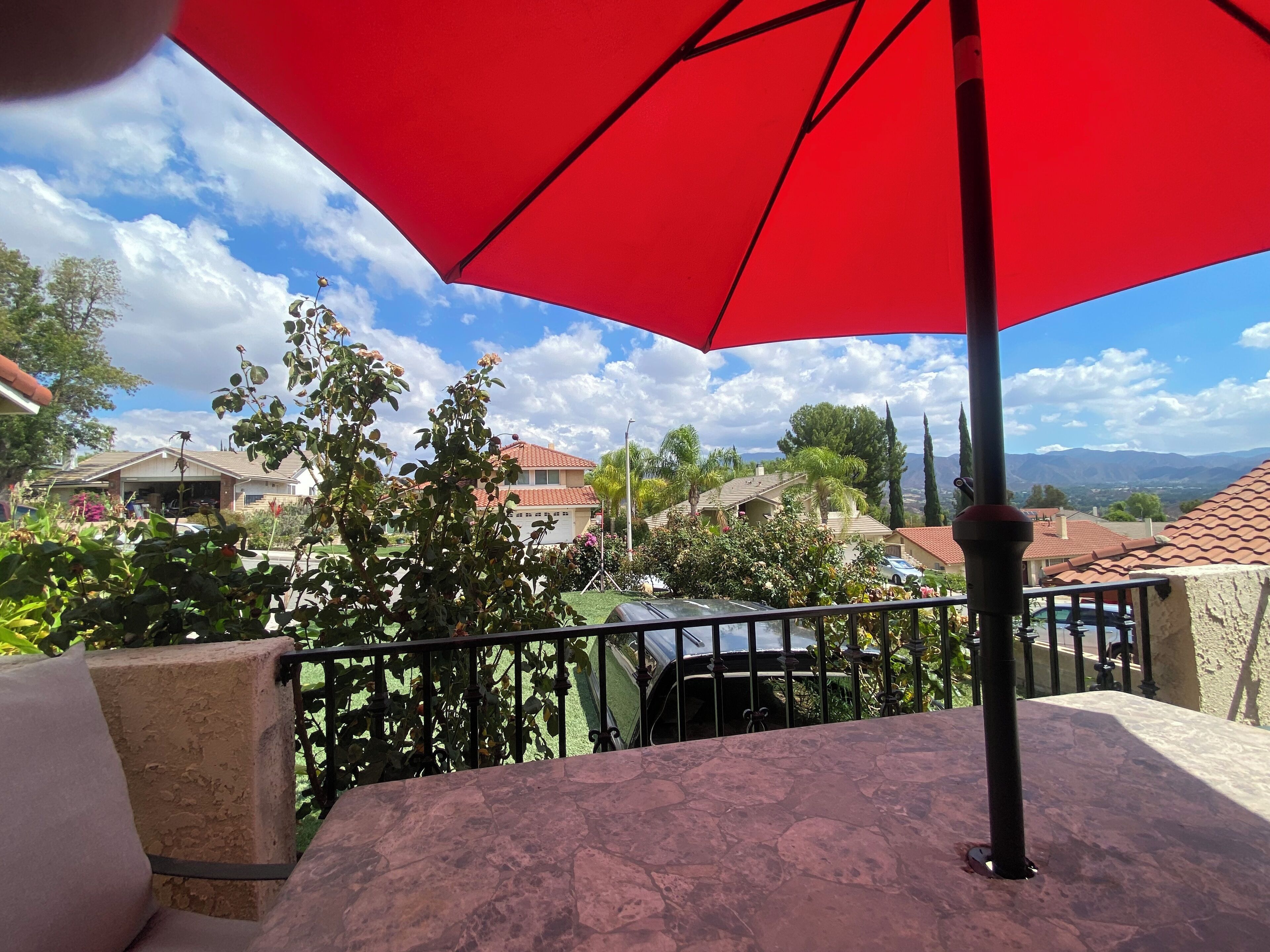 A terrace with a red umbrella, a stone table, and a view of houses and mountains.