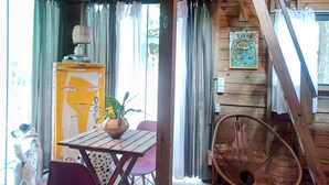 A rustic wooden interior with a dining table, chairs, a fan, and a dog.