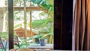 Una habitación con vista a un jardín, una cama con toallas y un ventanal con cortinas.