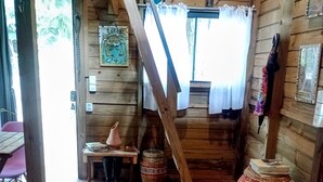 A rustic wooden cabin with a bed, a small table, and a staircase.