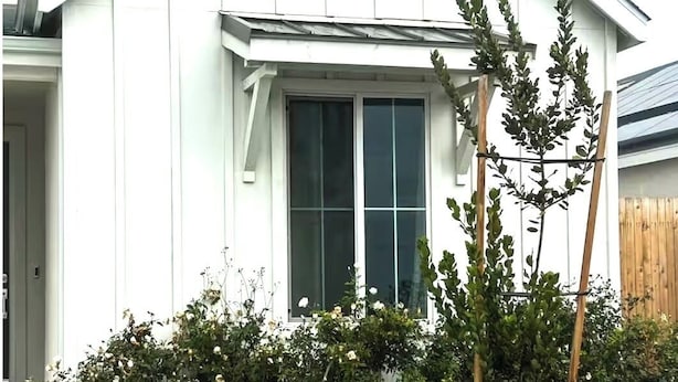 Une maison blanche avec une grande fenêtre et une clôture en bois en arrière-plan.