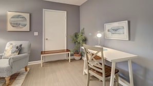 A room with a grey wall, a white door, a striped armchair, a white desk with a lamp, and a potted plant. - Spacious 3BR Hilton Head Getaway + Pool Access (Hilton Head Island)