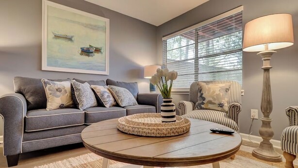 A living room with a grey sofa, a round coffee table, a striped armchair, and a floor lamp. - Spacious 3BR Hilton Head Getaway + Pool Access (Hilton Head Island)