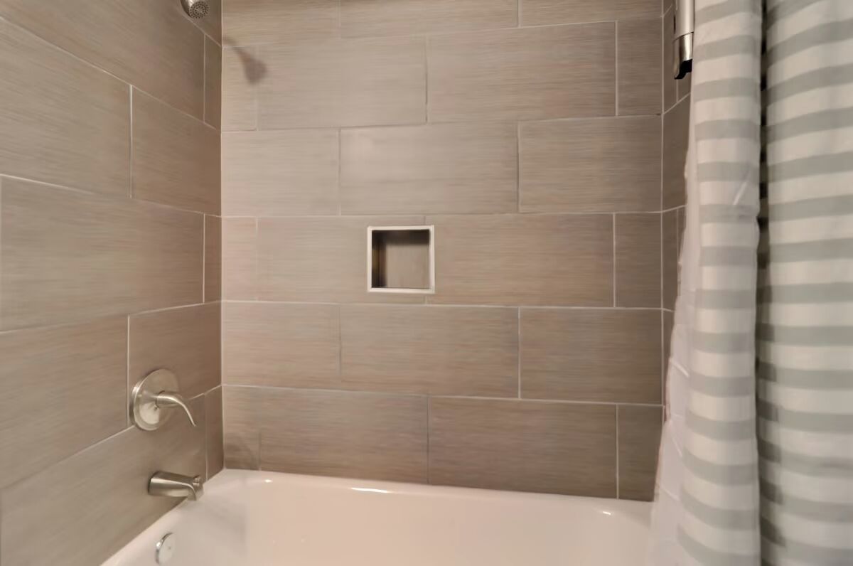 A modern bathroom with a bathtub, shower, and a small square tile feature on the wall.