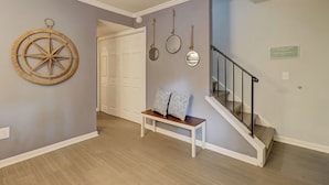 A hallway with a wooden bench, a wall-mounted compass, and a staircase with a black railing. - Spacious 3BR Hilton Head Getaway + Pool Access (Hilton Head Island)