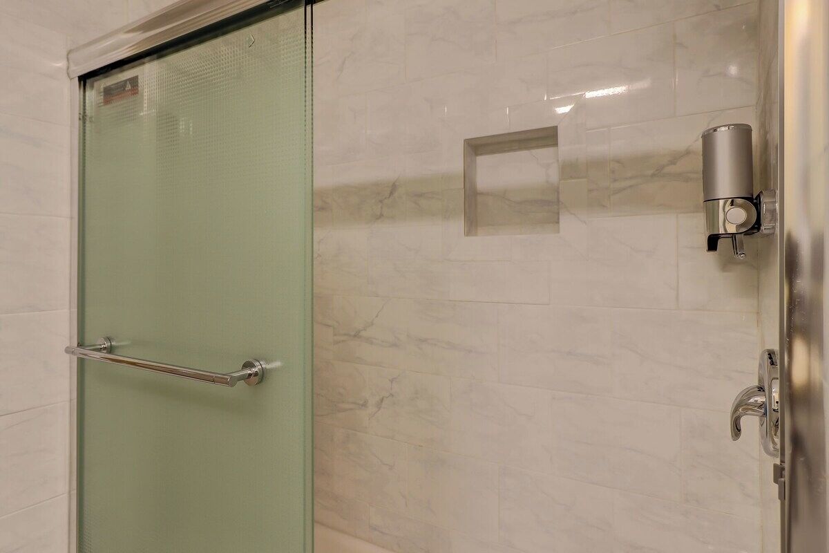 Un baño con puerta de cristal, barra para toallas y un secamanos instalado en la pared.
