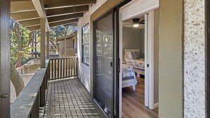 Eine überdachte Veranda mit Holzterrasse und eine Glasschiebetür zu einem Zimmer mit Bett und Deckenventilator.