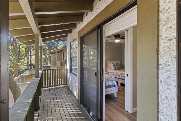 A covered porch with a wooden deck, a sliding glass door leading to a room with a bed and a ceiling fan. - Hilton Head 3BR Retreat Pool, Dining & Shops (Hilton Head Island)