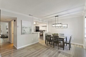A modern kitchen with white cabinetry, a dining area with a wooden table and chairs, and a large framed artwork on the wall. - Hilton Head 3BR Retreat Pool, Dining & Shops (Hilton Head Island)