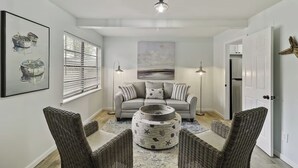 A modern living room with a grey sofa, wicker chairs, a round coffee table, and artwork on the walls.