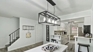 A modern kitchen with white cabinetry, a hanging light fixture, and a welcome sign.