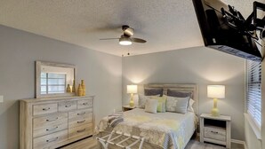 Een slaapkamer met een bed, nachtkastjes, een dressoir, een plafondventilator en een raam met jaloezieën.