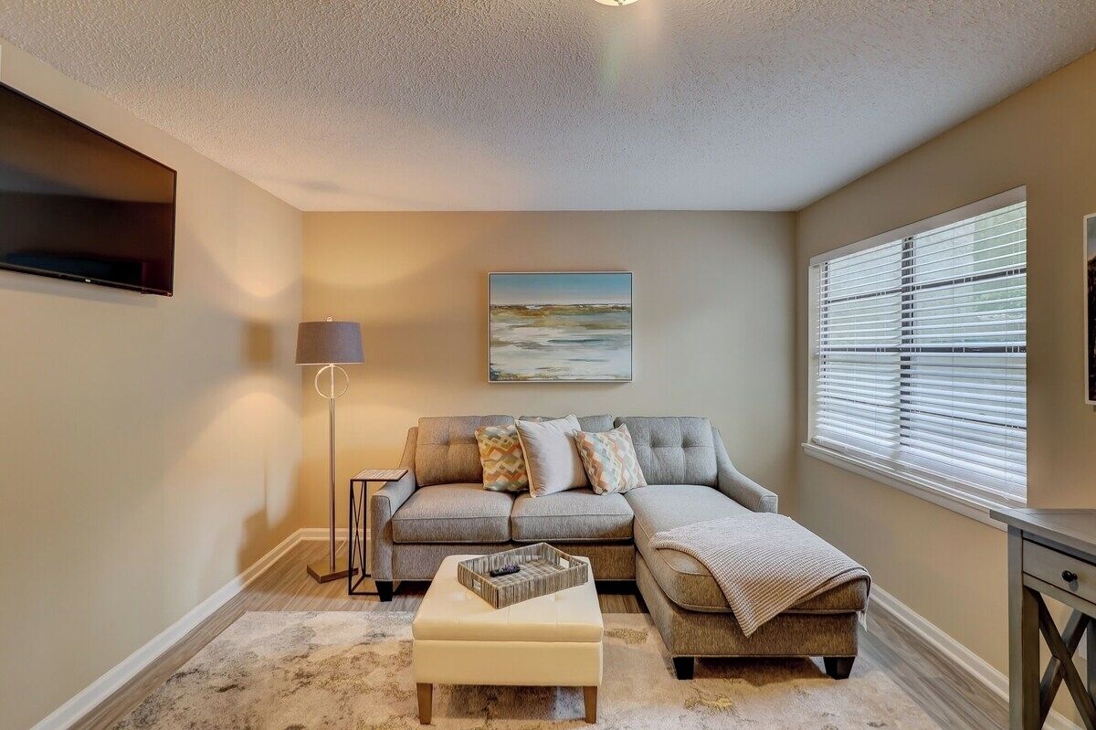 A living room with a sectional sofa, a floor lamp, a flat-screen TV, and a painting on the wall.