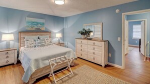 A bedroom with a bed, nightstands, a dresser, and a painting on the wall. - Beach Getaway 2BR w/ Pool + Modern Comforts (Hilton Head Island)