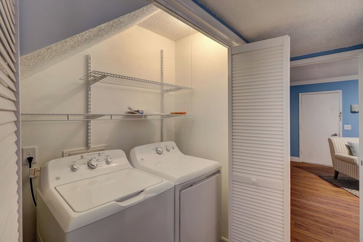 A laundry room with two white washers and dryers, metal shelves, and a white door leading to another room.