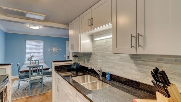 A modern kitchen with white cabinets, a granite countertop, and a built-in dishwasher. - Beach Getaway 2BR w/ Pool + Modern Comforts (Hilton Head Island)